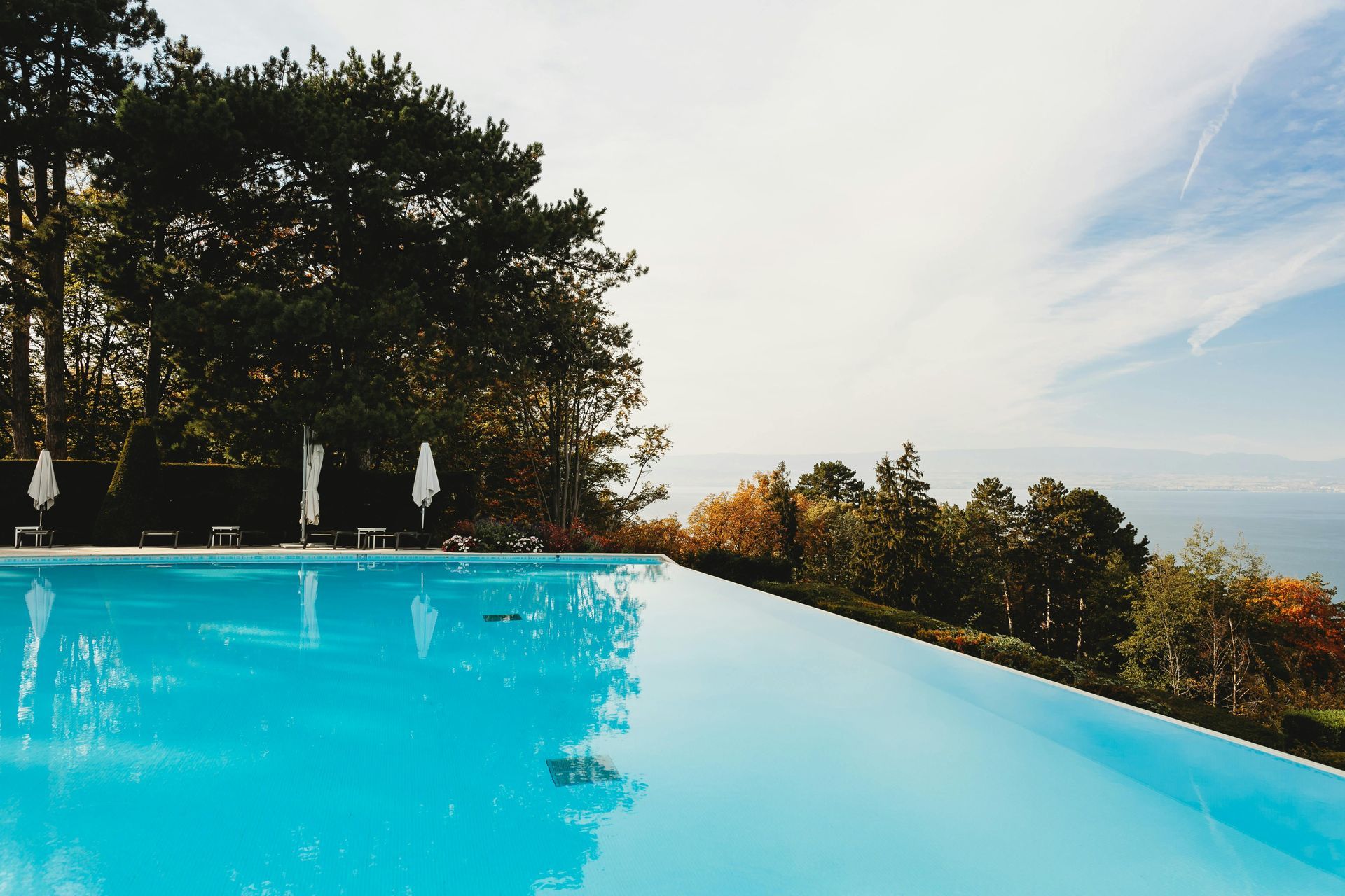 An infinity pool surrounded by trees and umbrellas with a view of the ocean.