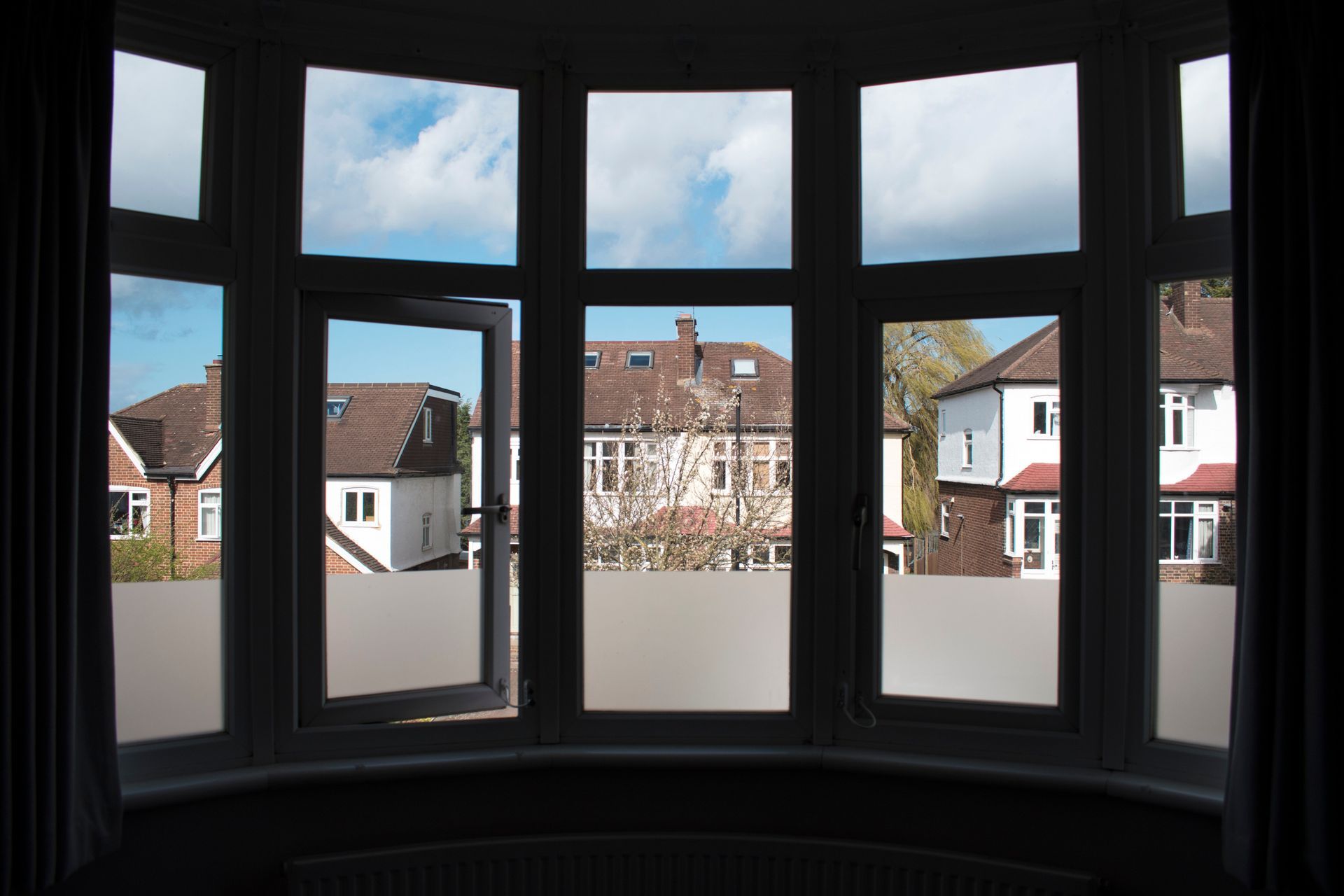The darkened interior of a bay window with a suburban view