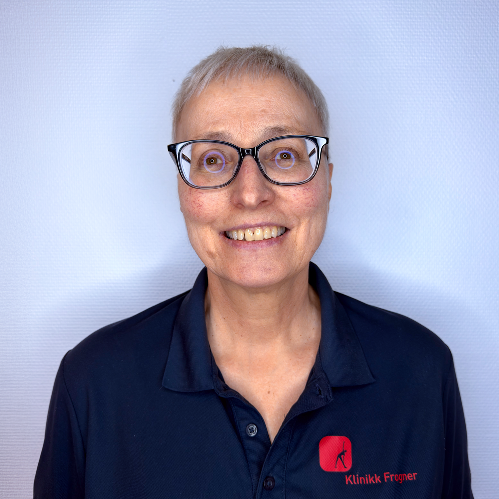 En smilende person med kort hår og briller, iført en marineblå poloskjorte med en liten rød logo, mot en lys vegg.