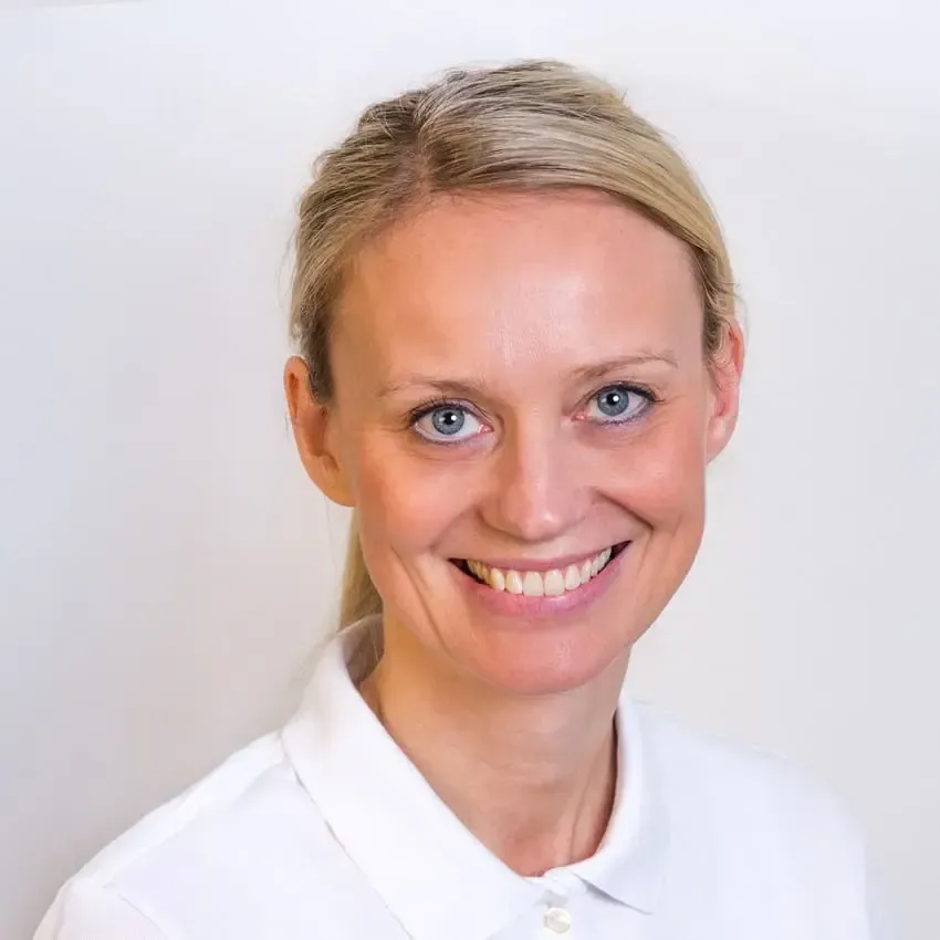 Kvinne med blondt hår som smiler, iført en hvit skjorte med krage.