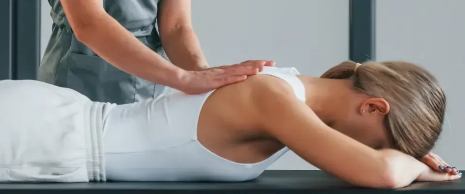 En person som får skuldermassasje ligger med ansiktet ned på et bord. En annen persons hender er på personens rygg.