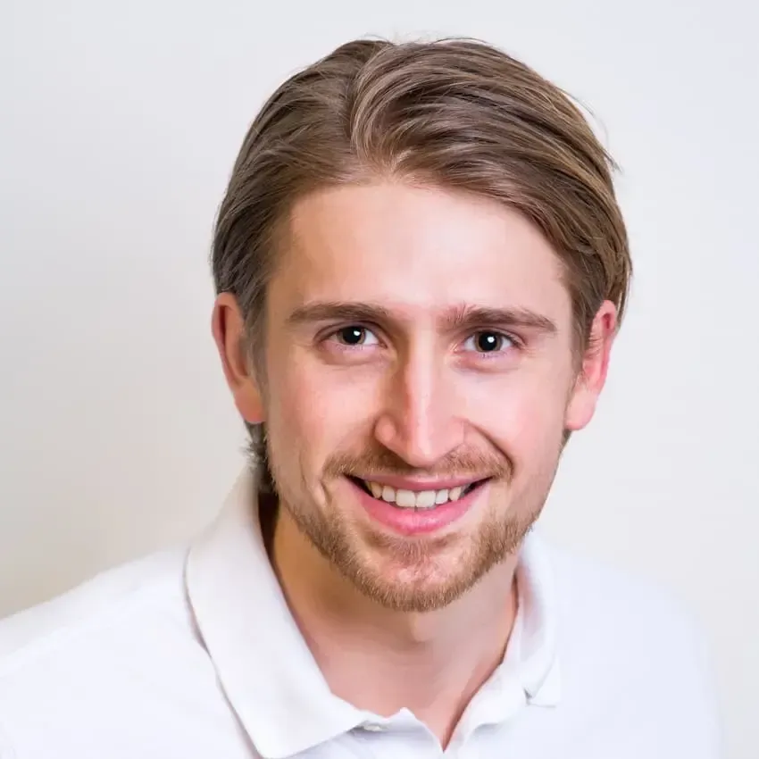 Smilende mann med lysebrunt hår i en hvit skjorte mot en ensfarget bakgrunn.