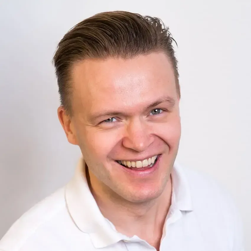 Mann med lys hud smiler, iført hvit skjorte.