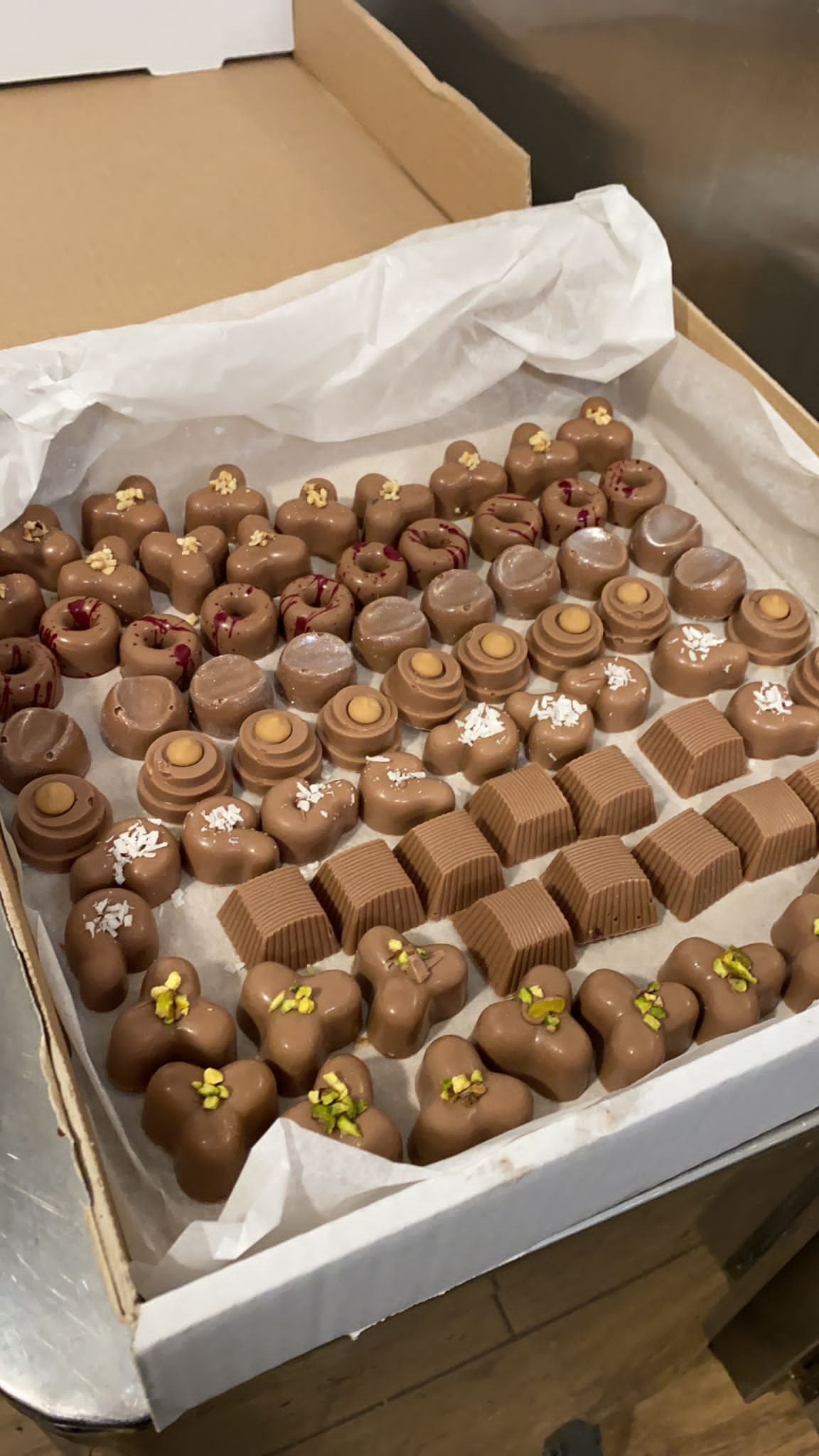 Scatola aperta piena di tartufi assortiti ricoperti di cioccolato e caramelle in pirottini di carta.