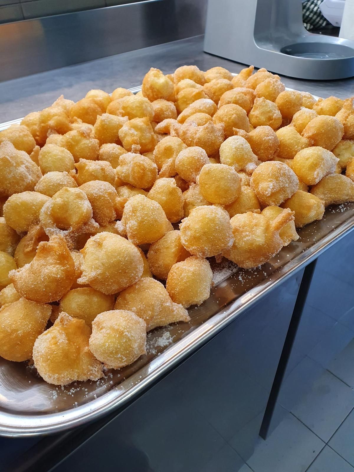 Vassoio di palline di pasta fritta dorata cosparse di zucchero su un bancone in acciaio inox