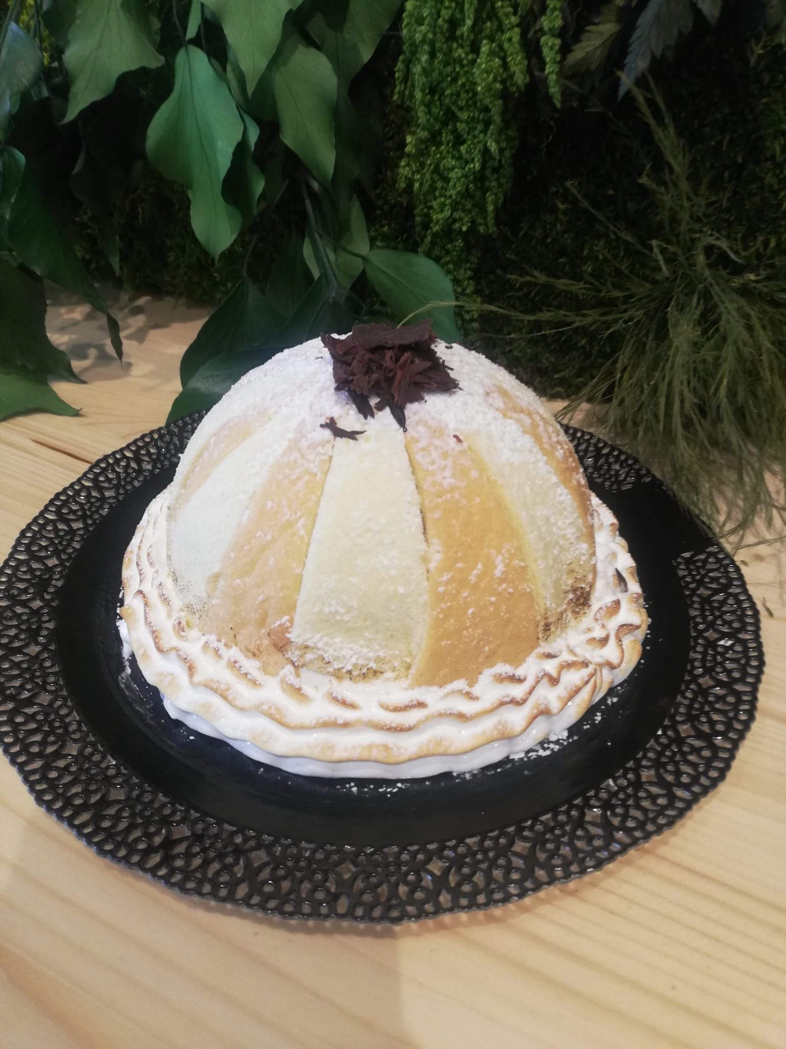 Torta a strati a forma di cupola con glassa bianca e copertura di cioccolato fondente su un piatto nero all'aperto