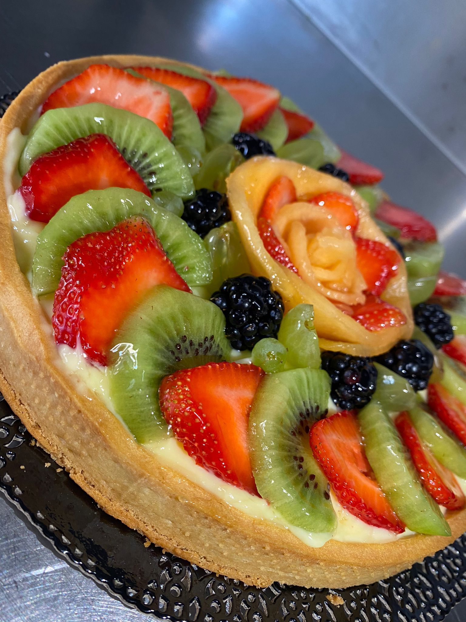 Crostata di frutta con kiwi, fragole, more e una rosa di pesca.