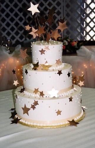 Torta nuziale bianca a tre piani con decorazioni a stella dorata su un tavolo.