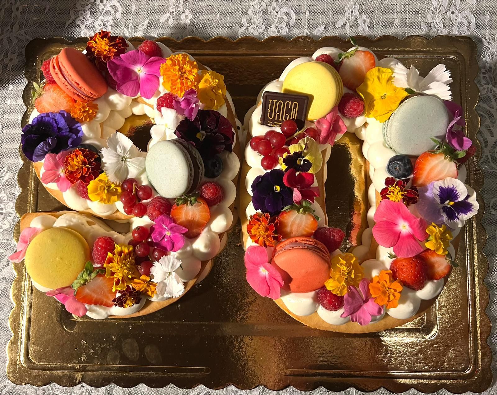 Dessert decorato a forma di numero 10, ricoperto di fiori colorati e macarons su un vassoio dorato.