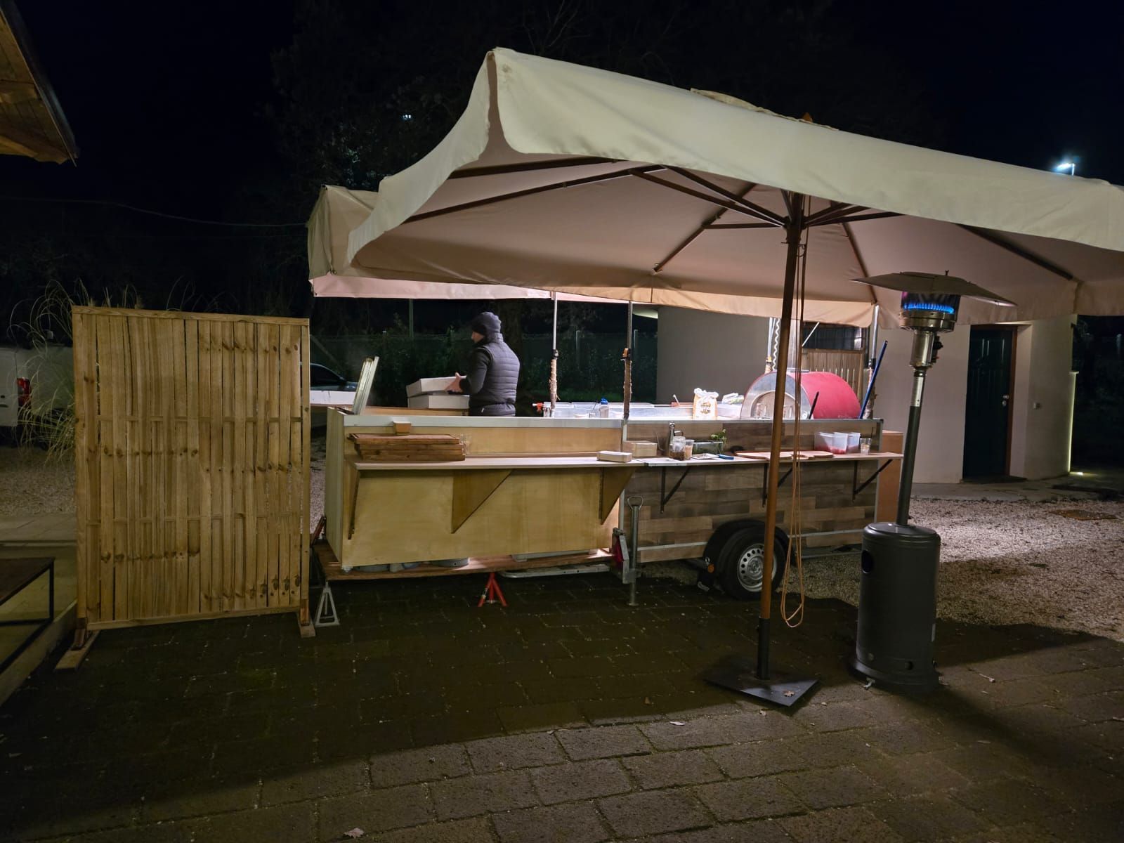 Chiosco di cibo notturno all'aperto sotto una tettoia bianca, con due persone che servono da un carretto di legno.