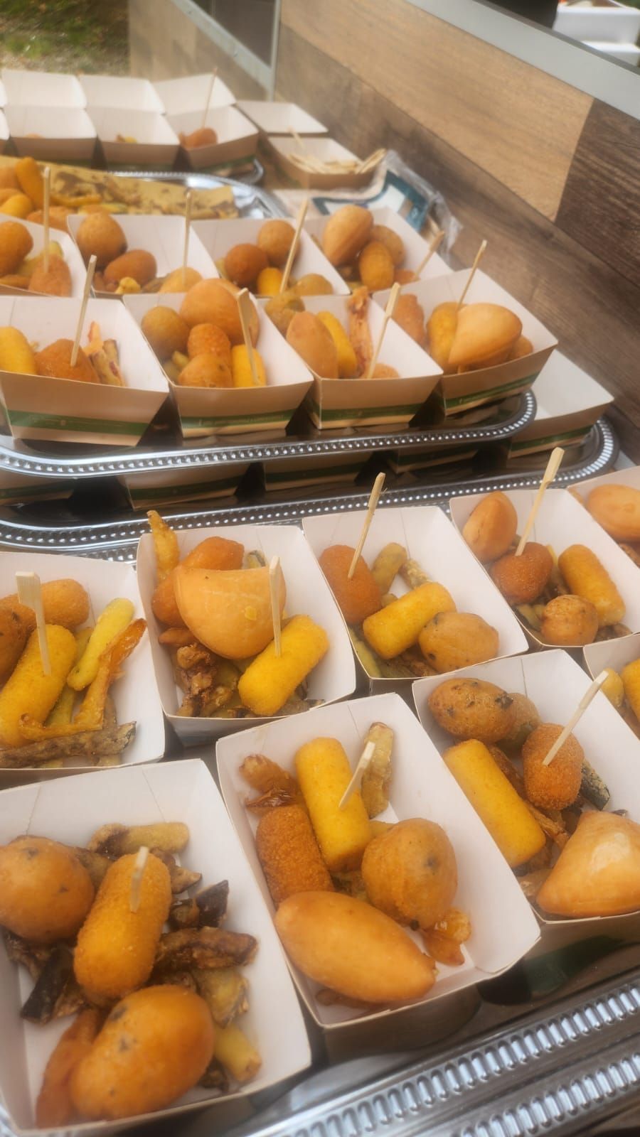 Vassoi di pasticcini fritti assortiti e snack dorati in una vetrina in stile mensa.