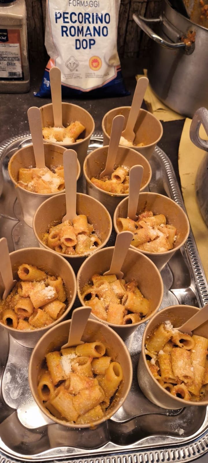 Piccole porzioni di rigatoni servite con cucchiaini di legno da degustazione, guarnite con pecorino romano grattugiato.