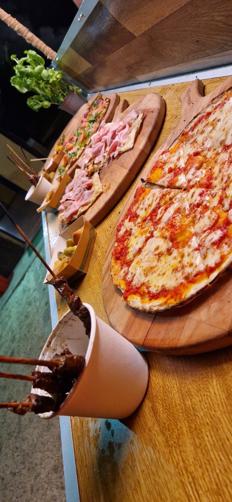 Un tavolo di legno con due pizze, una fetta su un piatto e bevande in un'accogliente atmosfera da ristorante.