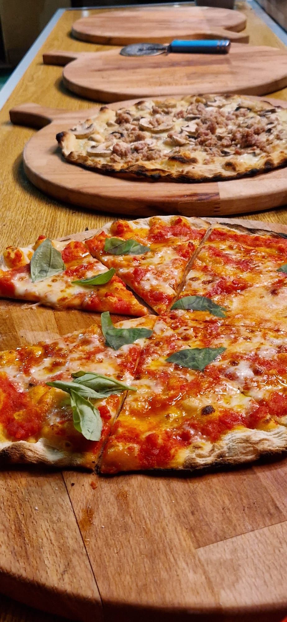 Tre pizze su taglieri di legno, tra cui una pizza al salame piccante davanti e una pizza ai funghi dietro.