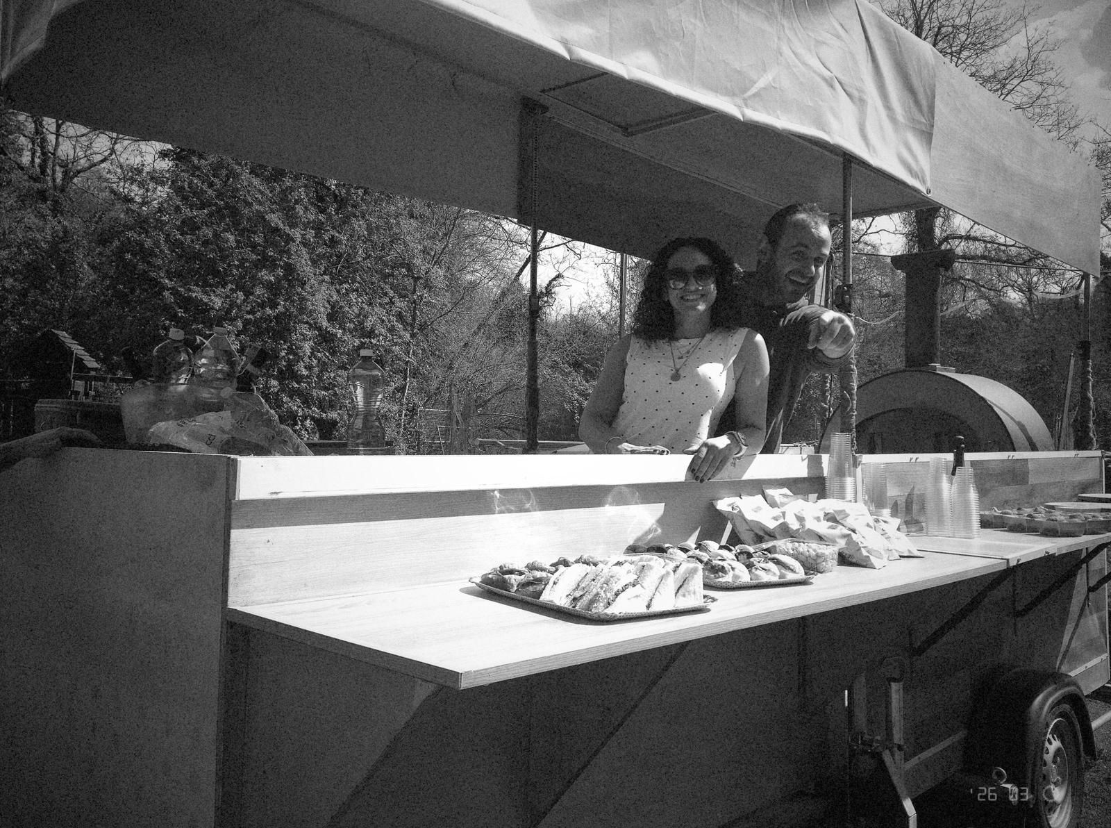 Due persone in piedi dietro un barbecue sotto una tettoia, con del cibo che cuoce all'aperto.
