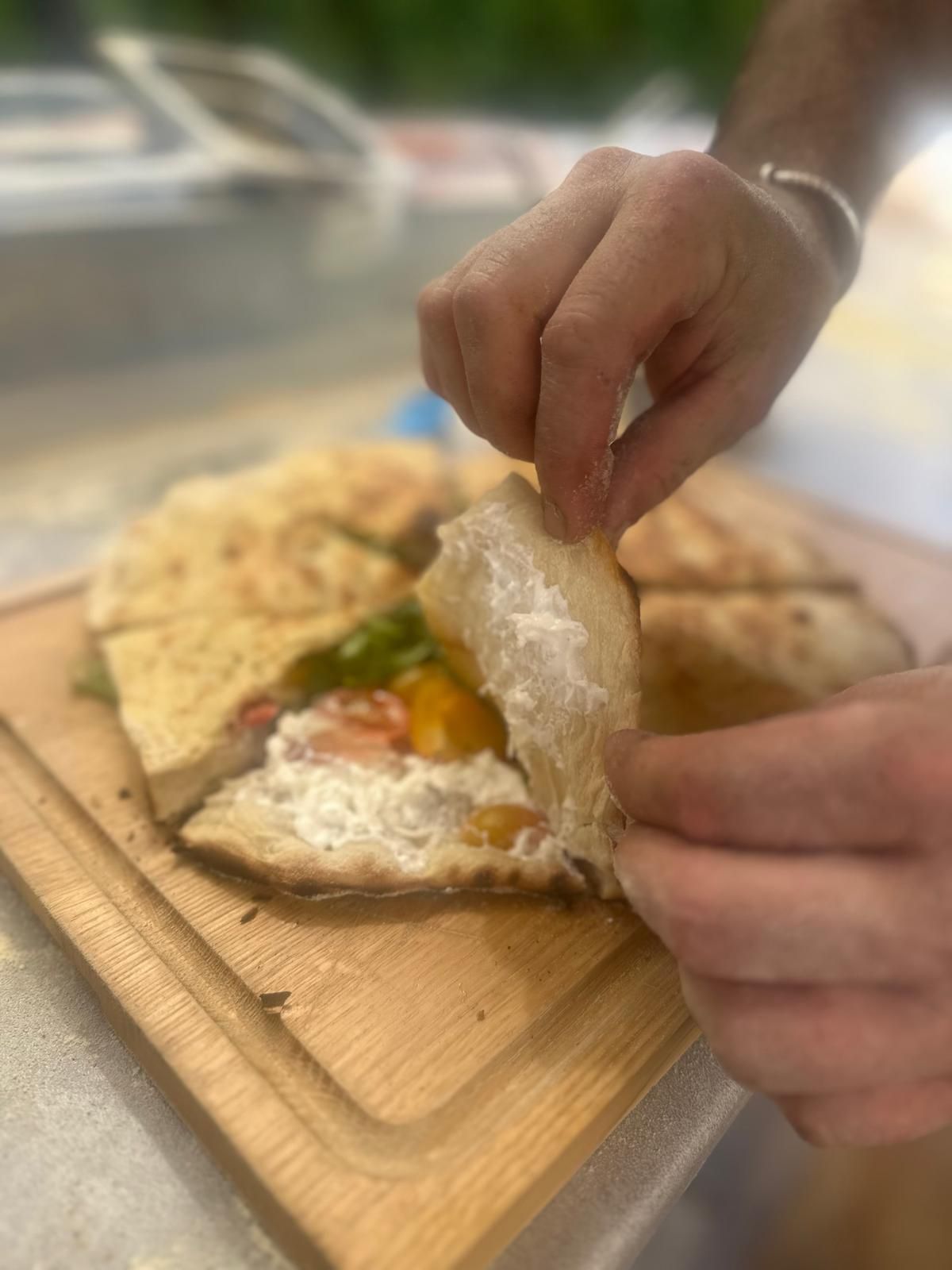 Mani che aprono un panino con pane piatto su un tagliere di legno all'aperto, con il ripieno cremoso ben visibile.