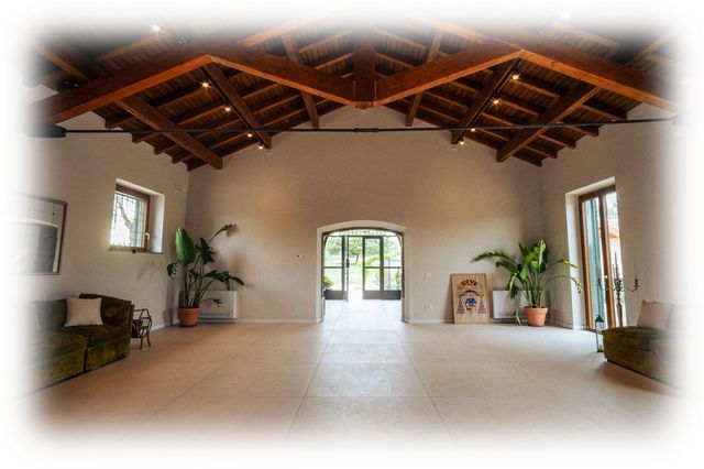 Ampia stanza vuota con soffitto in legno a vista, pareti bianche e porta ad arco che si affaccia su un giardino.