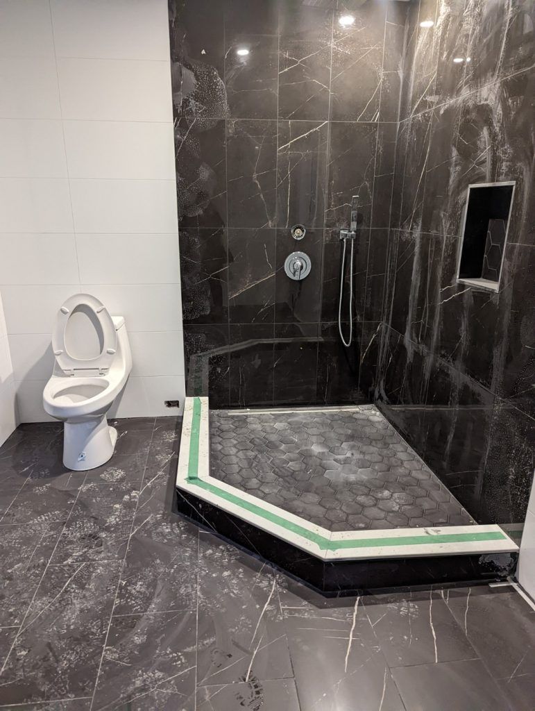 Bathroom under construction with black tile shower, toilet, and gray flooring.