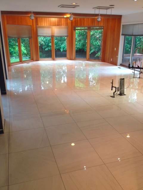 Large empty room with glossy tile floor, wood paneling, and large windows looking out to trees.