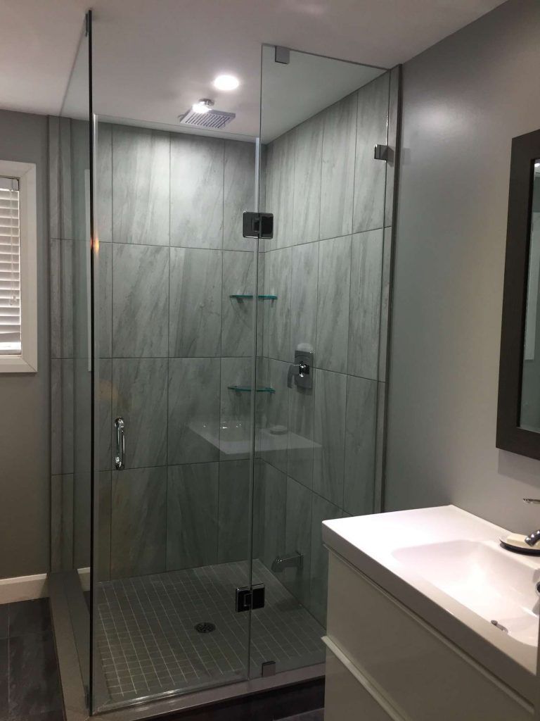 Glass shower enclosure in a modern bathroom with gray tile walls and white vanity.