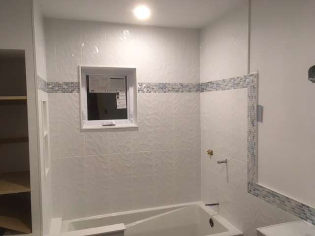 White-tiled bathroom with a bathtub, small window, and a decorative blue tile border.