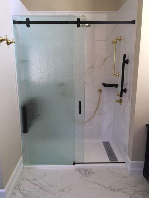 A modern shower with frosted sliding glass door and black hardware. White marble tile.