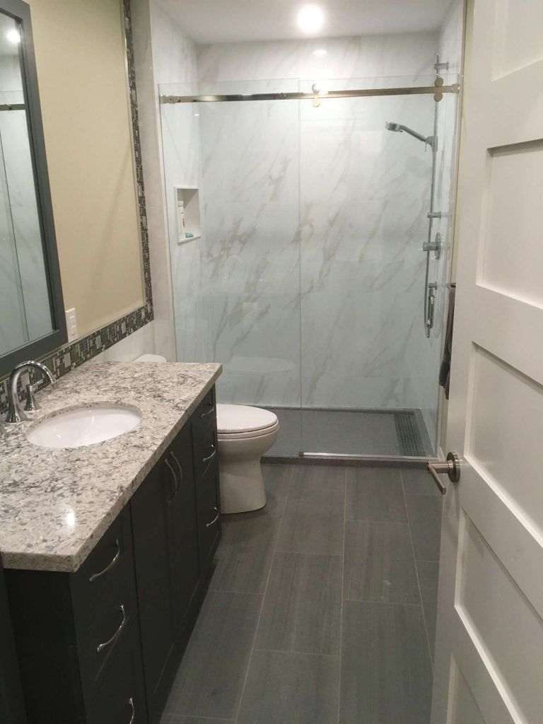 Modern bathroom with gray tile floor, marble-look shower, dark vanity, and white toilet.