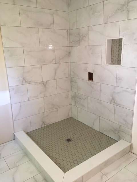 Newly tiled shower with marble-like walls, hexagonal floor, and a built-in shelf.
