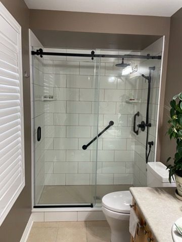 Bathroom shower with sliding glass doors, white subway tile, black fixtures, and a grab bar.