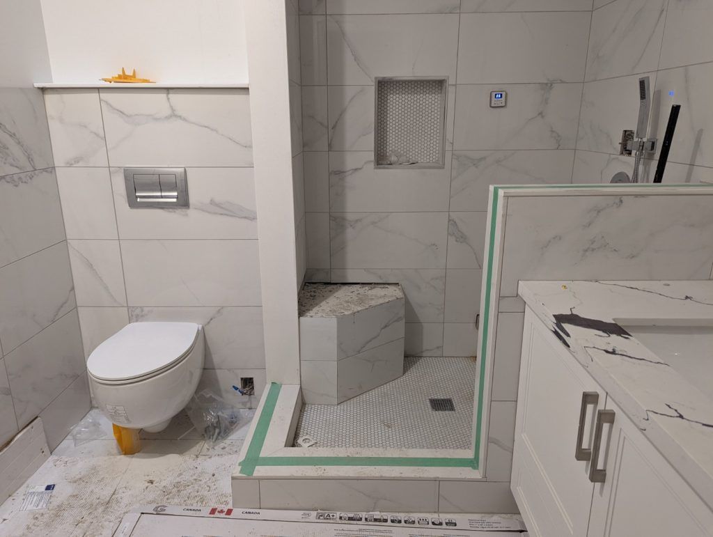 Bathroom under construction with white marble-like tiles, a toilet, shower, and vanity.