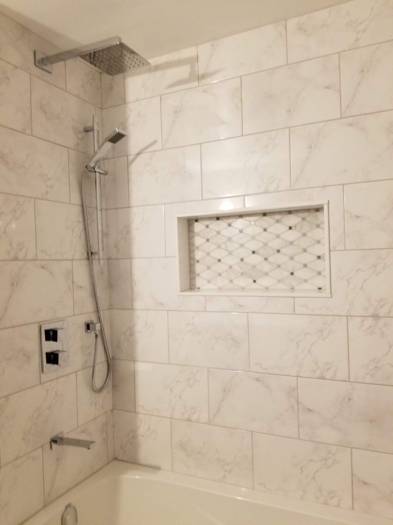 White tiled shower with built-in shelf. Silver shower head and faucet.