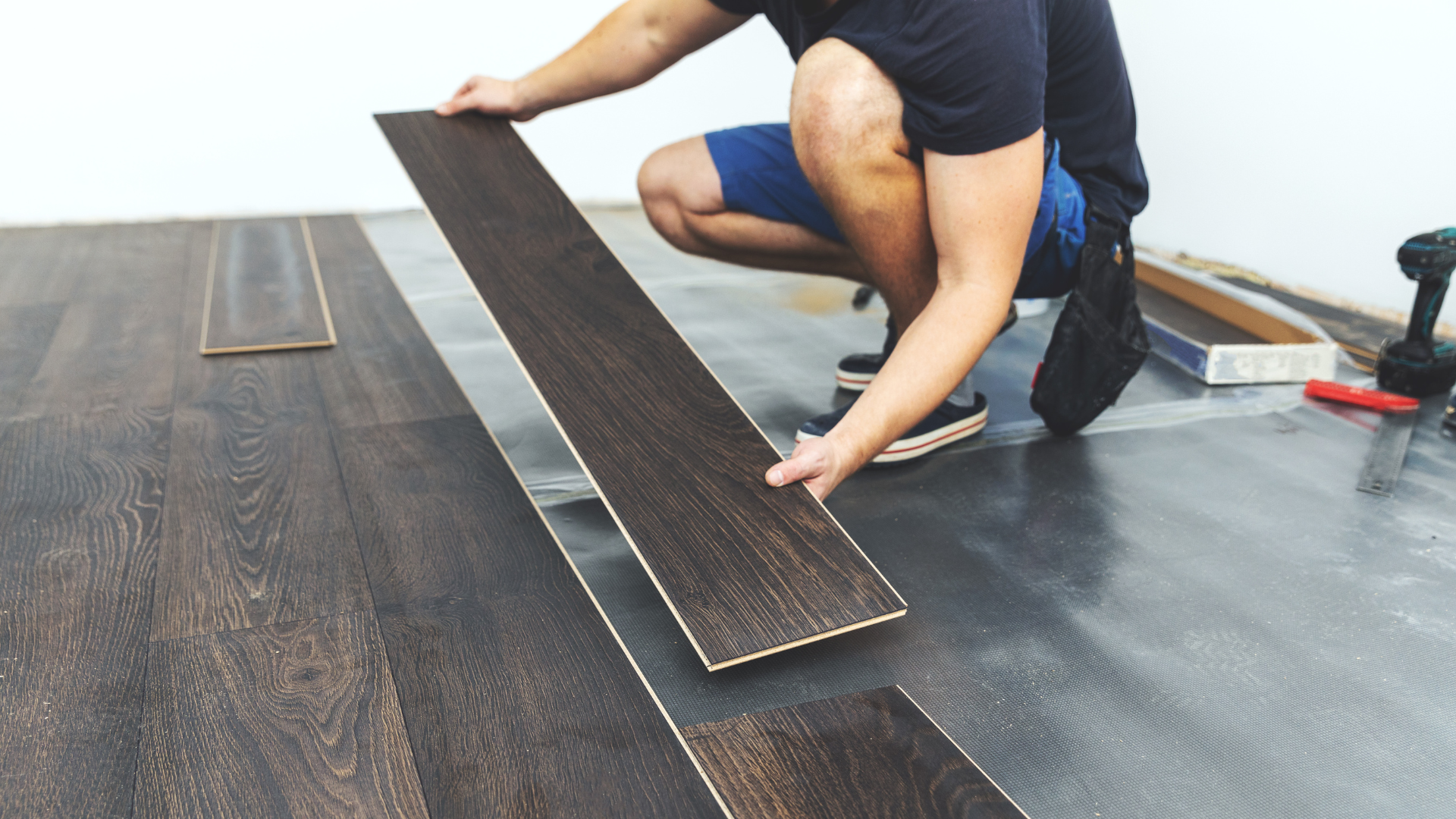 Person installing dark wooden floor planks in a room.