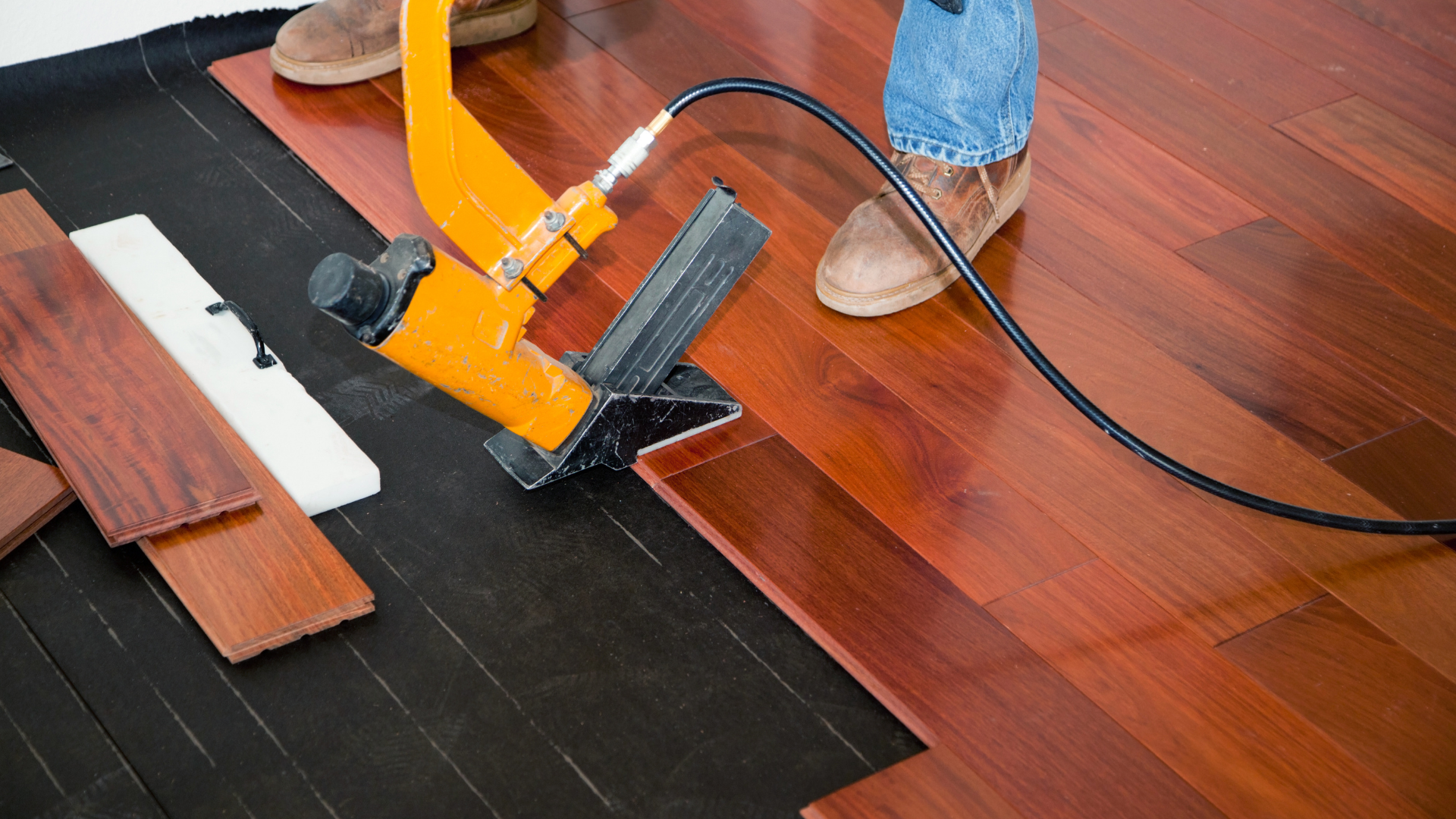 Person installing hardwood flooring using a pneumatic nailer.