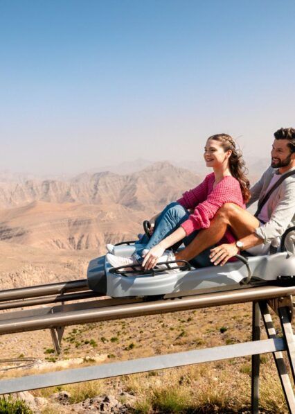 A man and a woman are riding a coaster on top of a mountain.