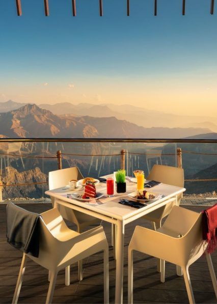 A table and chairs on a balcony with mountains in the background