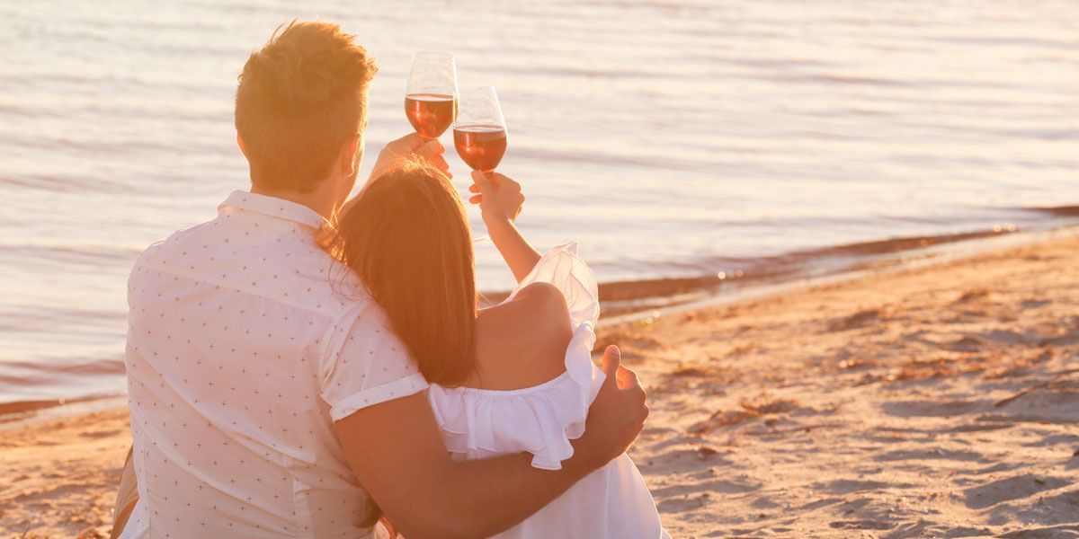 A man and a woman are sitting on the beach holding wine glasses.