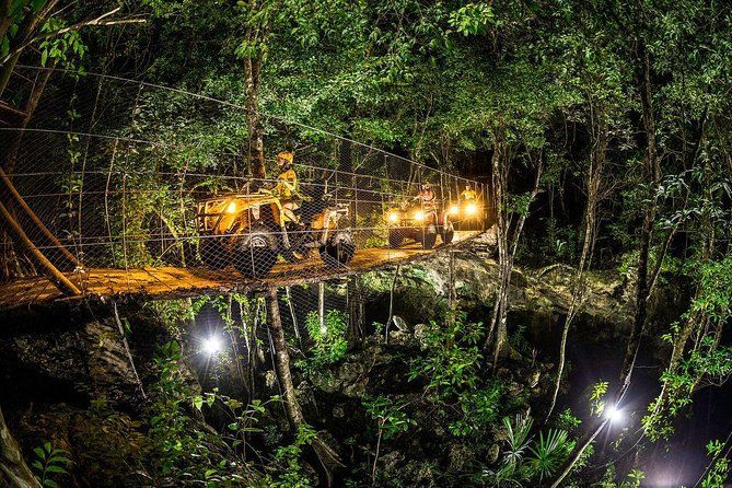 A group of vehicles are driving across a bridge in the woods at night.