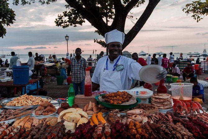 A man in a chef 's hat is standing in front of a table full of food.