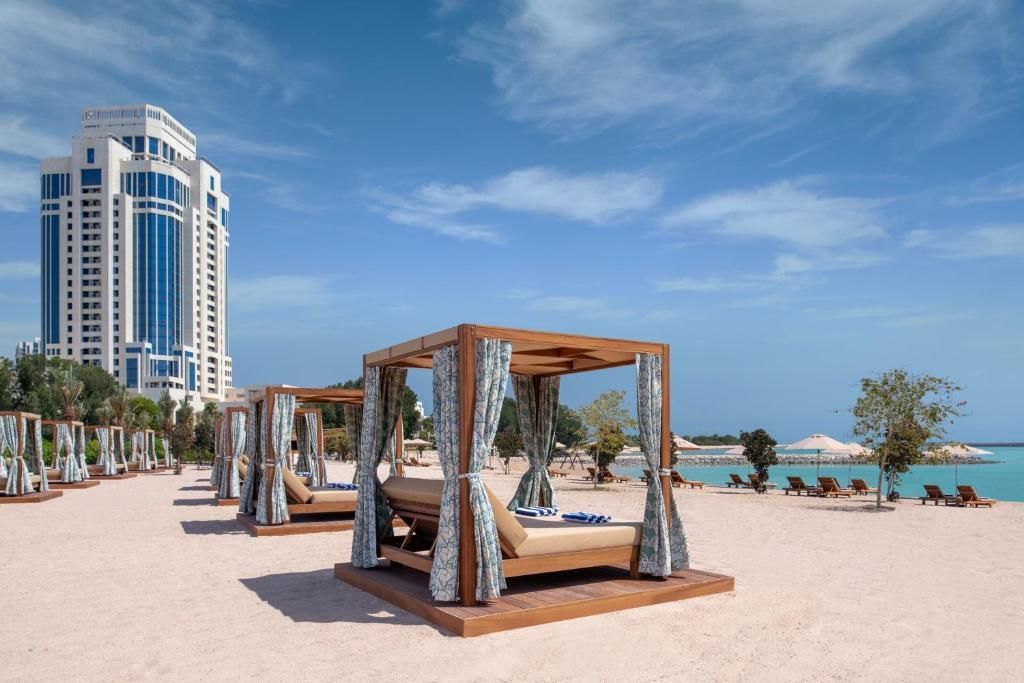 A row of beds on a beach with a tall building in the background.