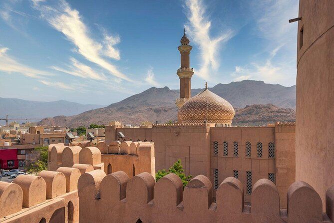 A castle with a mosque in the background and mountains in the background.