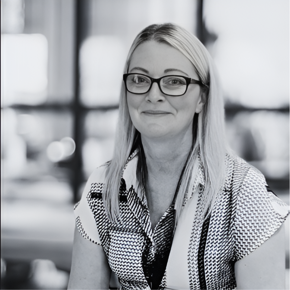 A woman wearing glasses is smiling in a black and white photo