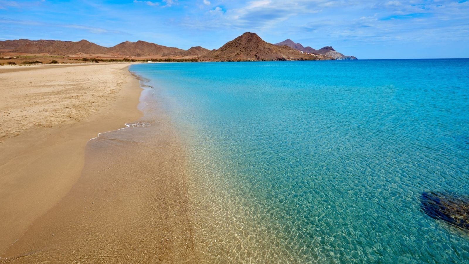 A beach with mountains in the background and a clear blue ocean.