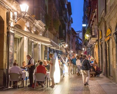 A group of people are sitting at tables outside of a restaurant.