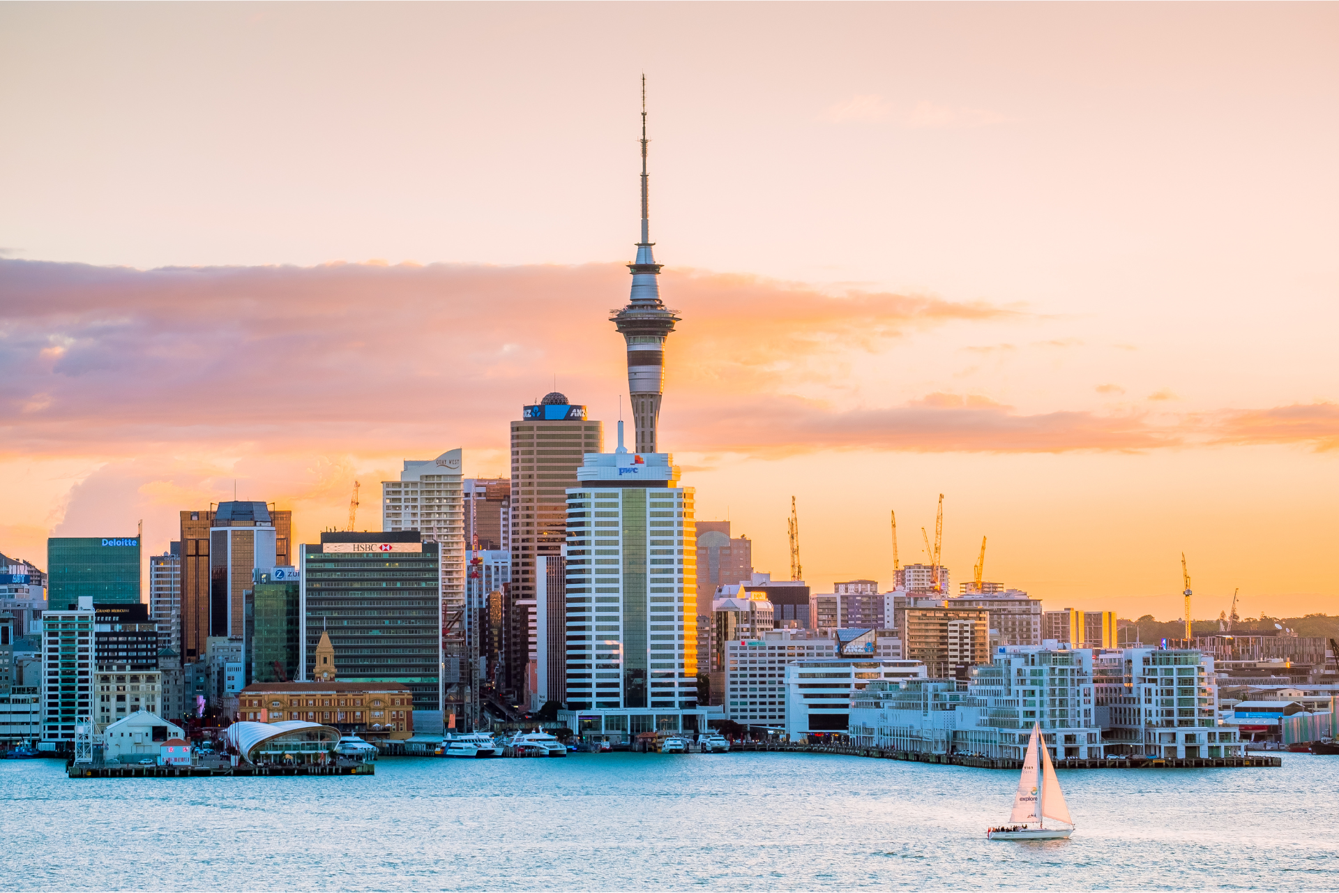 A sailboat is floating in front of a city skyline at sunset.