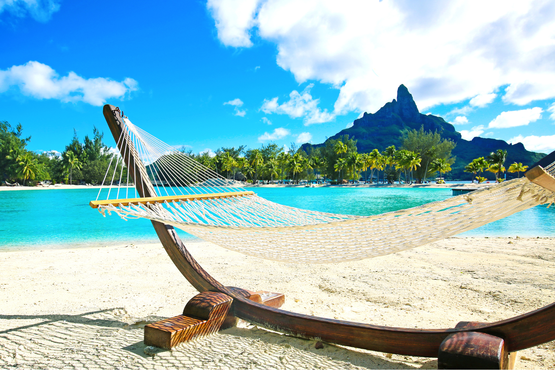 A hammock is sitting on a sandy beach next to a body of water.