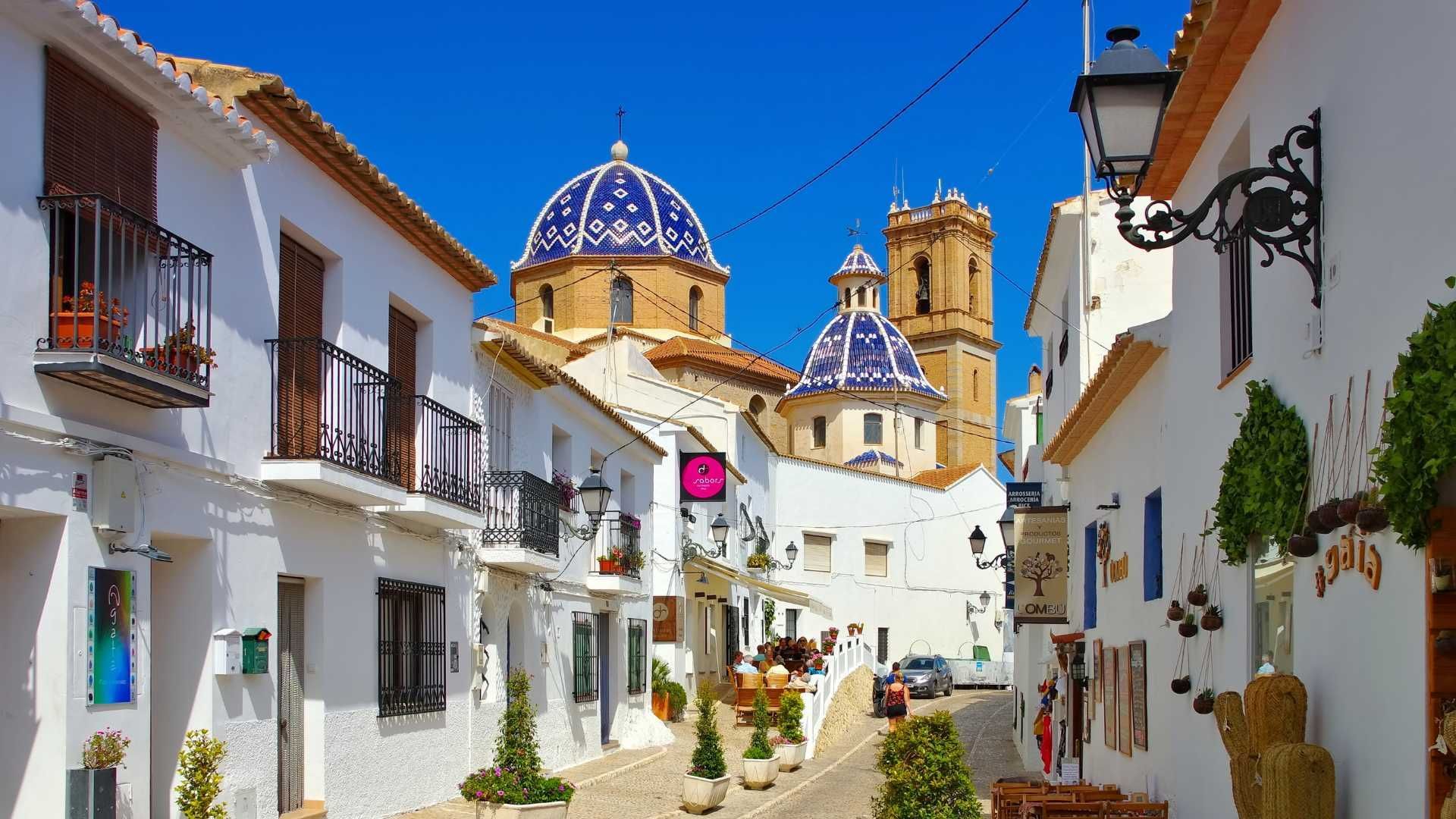 A narrow street in a small town with a church in the background.