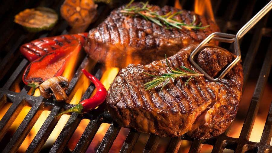 A steak is being cooked on a grill with flames coming out of it.