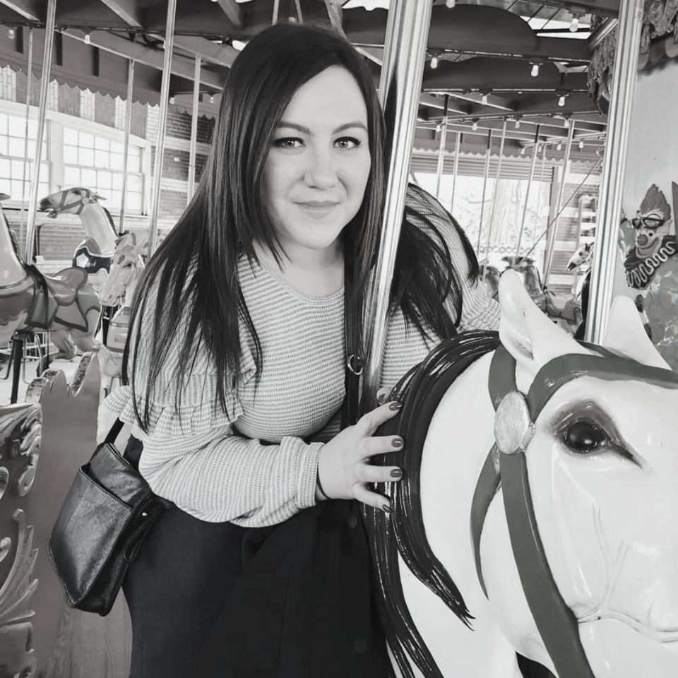 A woman is standing next to a carousel horse in a black and white photo.