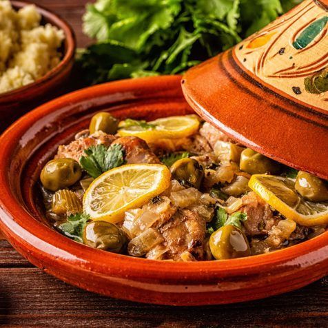 A bowl of food with lemon slices and olives on a wooden table.