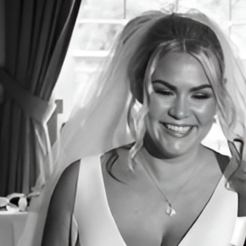 A woman in a wedding dress and veil is smiling in a black and white photo.